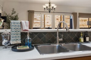 A kitchen with a double sink, a chandelier, and a window with wooden shutters. - Luxury French-Inspired Retreat • Private Terrace (Kelowna)