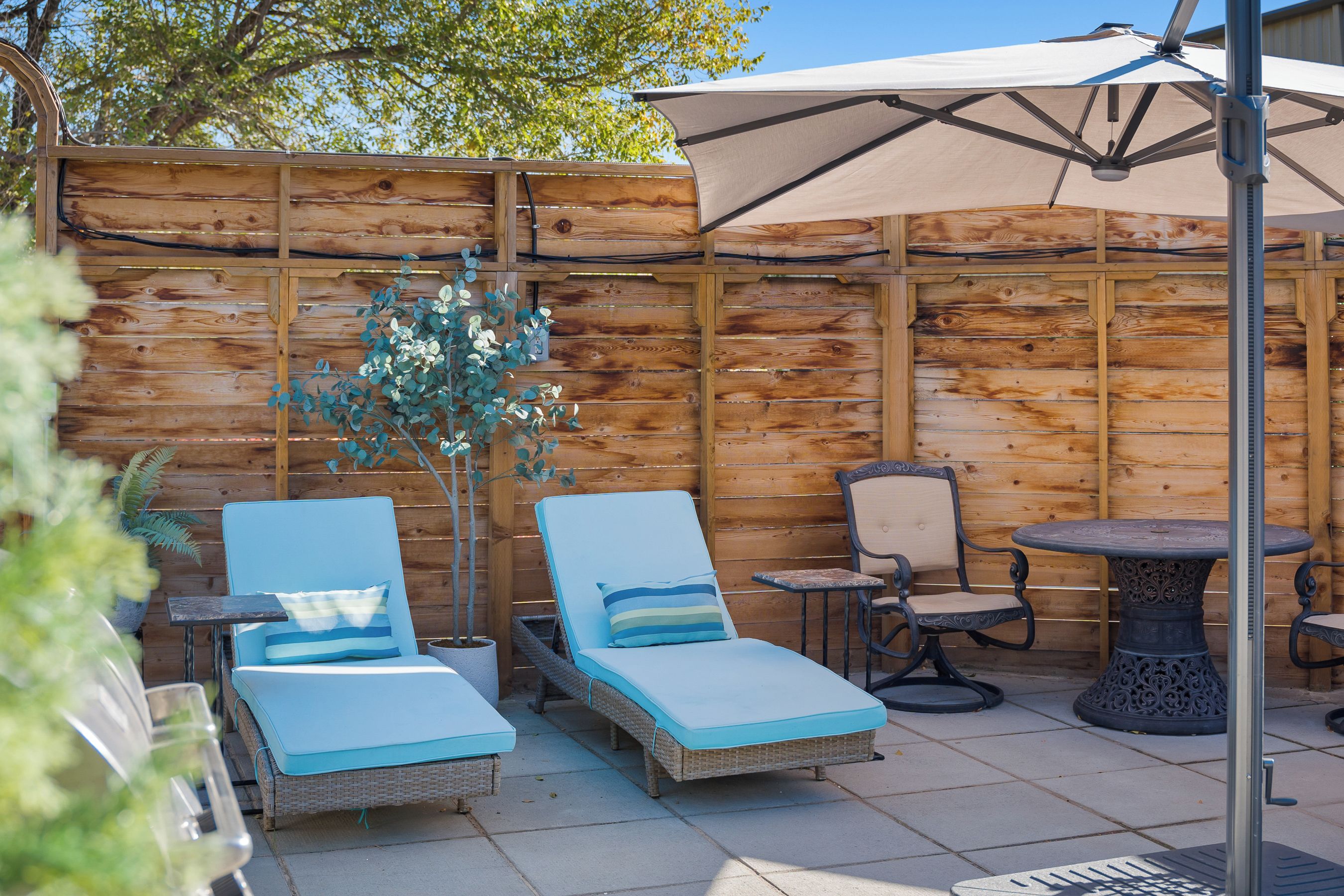 An outdoor patio with two lounge chairs, a small table, and a decorative umbrella.