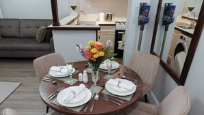 Un comedor con una mesa redonda para cuatro personas, un florero con flores y una cocina al fondo.