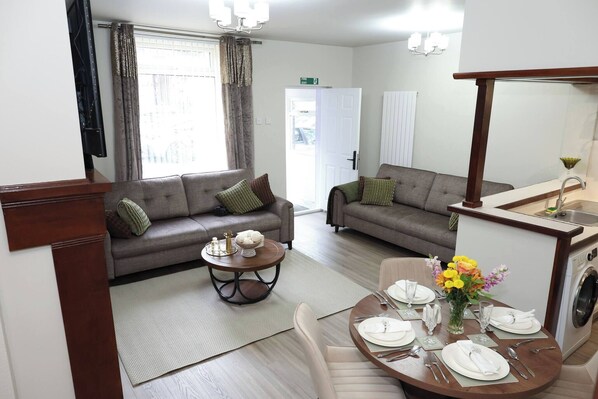 Una sala moderna con dos sofás, una mesa de comedor para cuatro personas y una cocina con lavaplatos y lavadora.