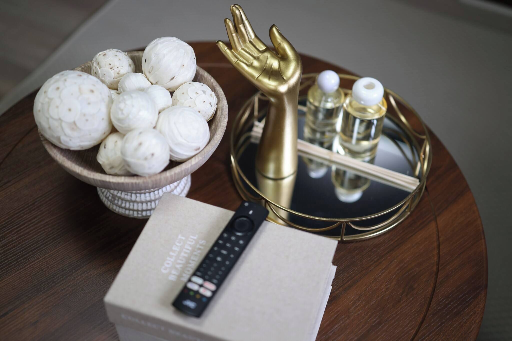 A tray with a bowl of white eggs, a golden hand-shaped object, a remote control, and two bottles on a wooden surface.