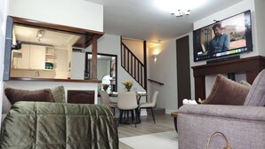 Una sala moderna con televisor de pantalla plana, un sofá, una mesa de comedor con sillas, una escalera y una zona de cocina.