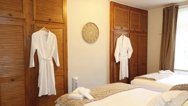 Habitación de hotel con paneles de madera, dos camas con ropa blanca, un reloj de pared y una ventana con cortinas.