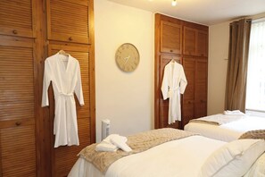 Habitación de hotel con paneles de madera, dos camas con ropa blanca, un reloj de pared y una ventana con cortinas.
