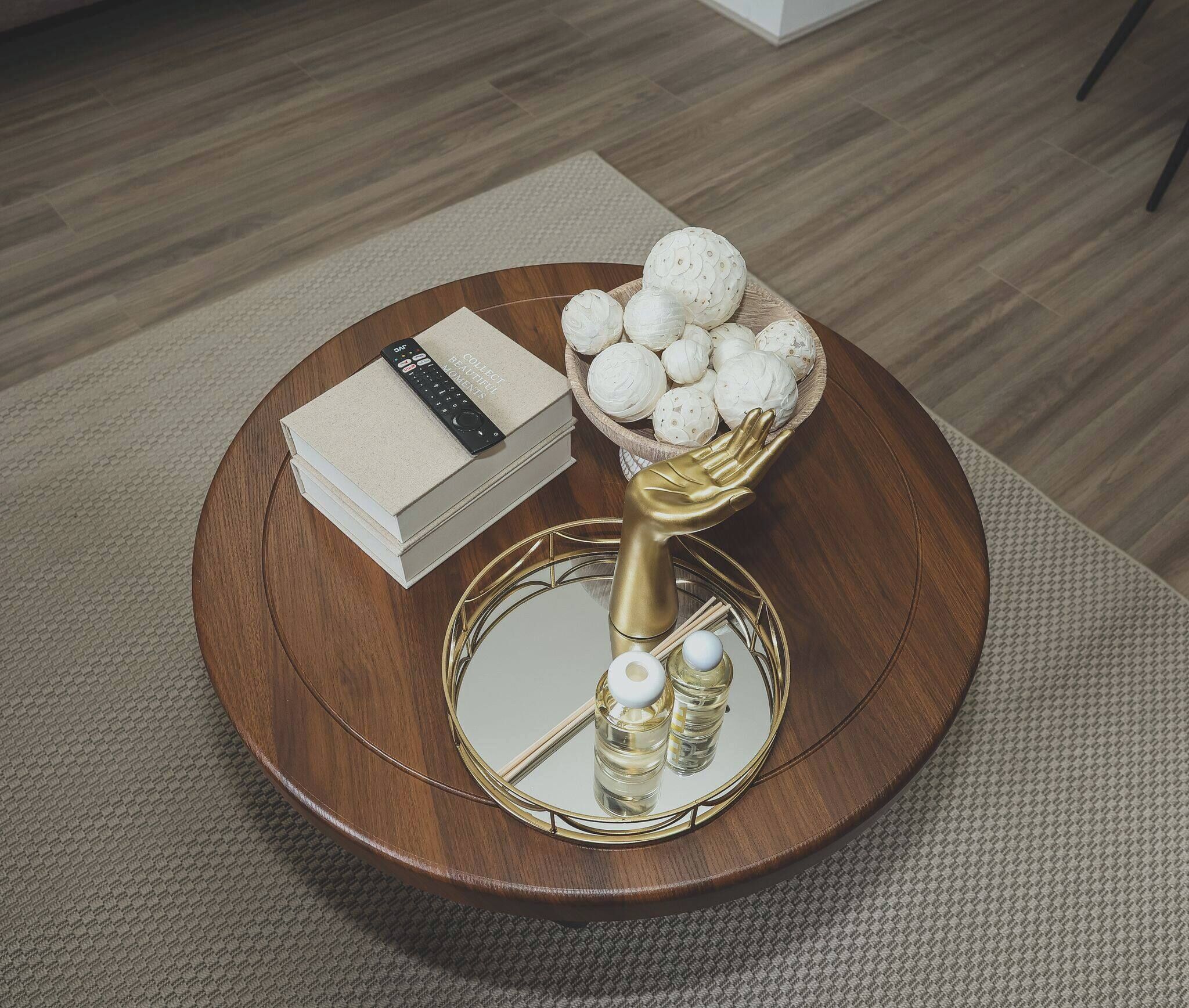 A round wooden table with a mirror, a book, and a bowl of decorative items.