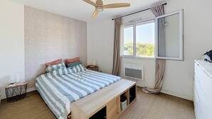 Una camera da letto con un letto, una ventola a soffitto, una finestra con tende, un comodino e una cassettiera.