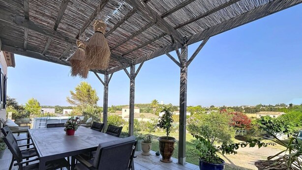 Un portico coperto con tavolo e sedie, piante in vaso e vista sulla campagna.