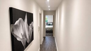 Un pasillo con un gran cuadro abstracto a la izquierda, una puerta que da a un dormitorio y suelo de madera.
