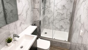 Un baño moderno con ducha envuelta en vidrio, un lavabo blanco y un espejo grande.