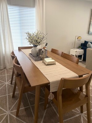Un comedor con una mesa de madera, sillas, un florero, una botella y una bandeja.