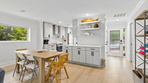 Una cocina moderna con armarios blancos, una mesa de comedor de madera y vistas a zonas verdes.