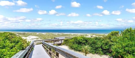 Un muelle de madera que lleva a una playa con vista clara al océano y un paisaje arenoso.