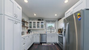 A modern kitchen with white cabinets, stainless steel appliances, and a wooden floor. - Aspen Run Condo Unit 29A (Ruidoso)