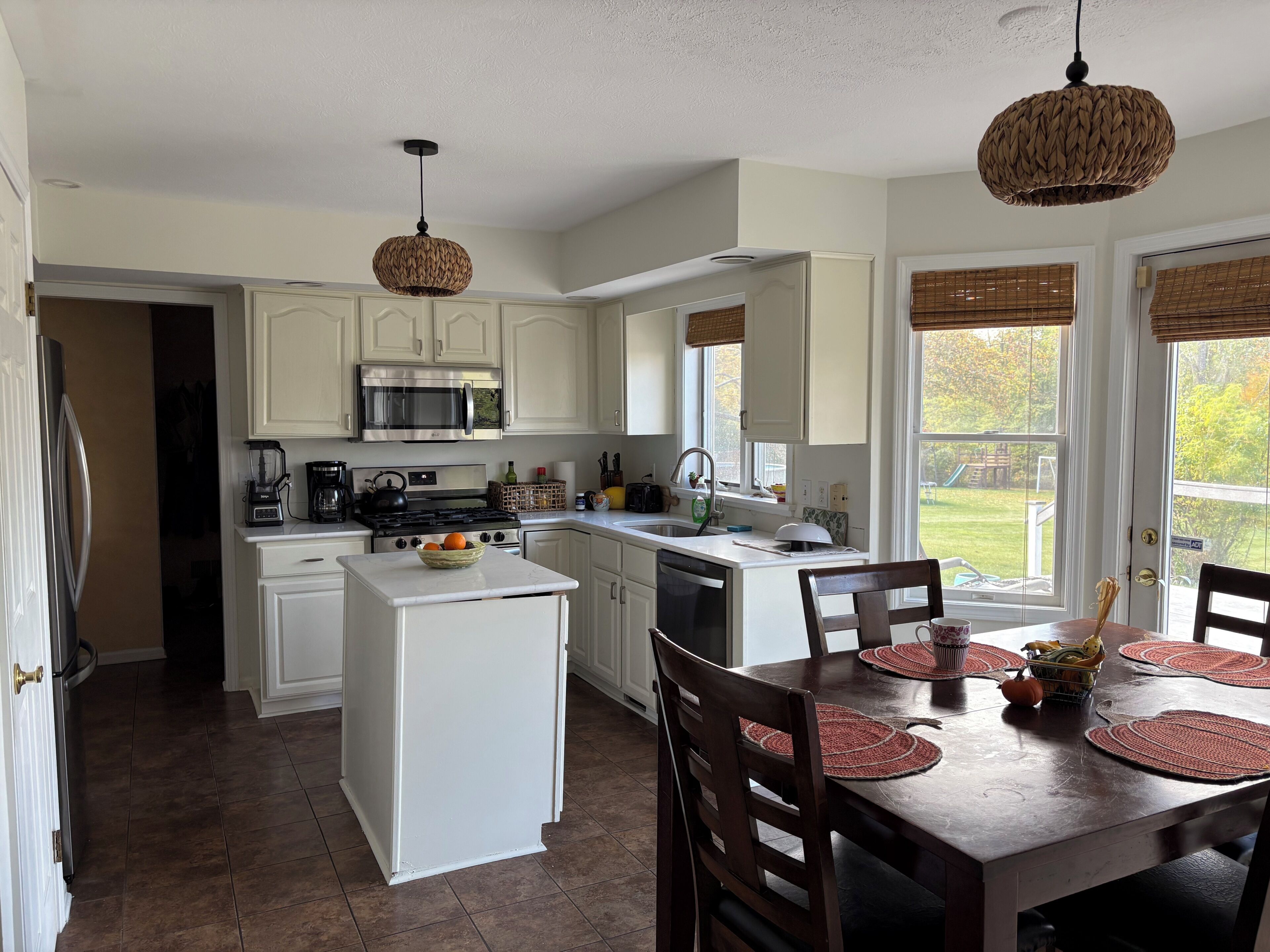 A kitchen with white cabinets, a central island, a dining table with chairs, and a view of the outdoors.
