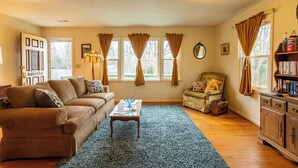 A living room with a sofa, a coffee table, a chair, a bookshelf, and a window with curtains.
