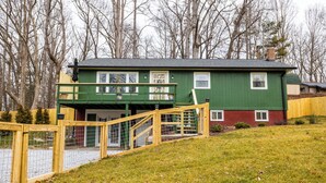 A green house with a balcony, a wooden fence, and a grassy yard.