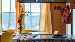 A kitchen with a stove, oven, wooden cabinets, and a window with curtains.