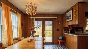 A wooden interior with a dining table, chairs, a vase with flowers, a television on a small table, and a kitchen area with a stove and cabinets.