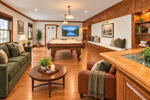 A room with a pool table, green sofa, wooden coffee table, and a bar area with a wooden countertop.