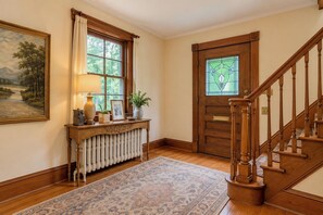 A hallway with a wooden staircase, a radiator, a console table with decorative items, and a painting on the wall. - The Historic Colombia Manor, Near Washington DC, w/lots of comfort/elegancy (Silver Spring)