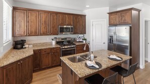 A kitchen with wooden cabinets, a stainless steel refrigerator, a microwave, and a granite countertop. - Family Friendly Poolside Home near Zion & Sand Hollow (Washington)