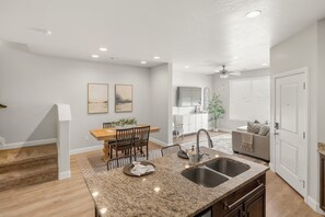 Una cocina moderna con encimeras de granito, un lavaplatos y un comedor con mesa y sillas de madera.