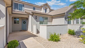 A two-story house with a front porch, a door with a wreath, and a small garden with gravel and plants. - Family Friendly Poolside Home near Zion & Sand Hollow (Washington)
