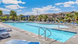 A swimming pool with lounge chairs and palm trees, surrounded by buildings. - Family Friendly Poolside Home near Zion & Sand Hollow (Washington)