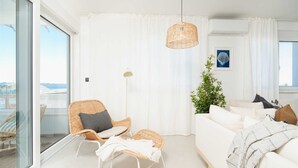 Ein modernes Wohnzimmer mit einem weißen Sofa, Korbstühlen, einer Stehlampe und Blick durch große Fenster.