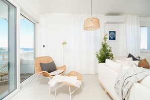Ein modernes Wohnzimmer mit einem weißen Sofa, Korbstühlen, einer Stehlampe und Blick durch große Fenster.