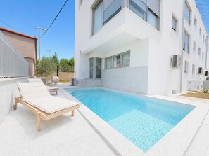 A modern building with a swimming pool, lounge chairs, and a clear sky. - Villa Galeb - Apartment with Private Pool and Sea View (Petrčane (Zadar))
