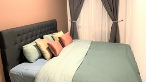 Ein Schlafzimmer mit einer gesteppten Kopfteile, einem Bett mit einer Bettdecke in Grün und Blau und zwei Vorhängen.