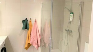 Ein modernes Badezimmer mit Duschkabine aus Glas, einem sichtbaren Handtrockner und einem wandmontierten Handtuchhalter mit mehreren Handtüchern.