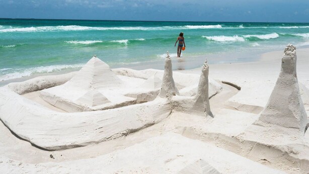 Ein Sandstrand mit einer Person, die auf das Meer zugeht.