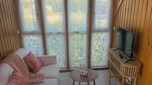 A room with a white sofa, an orange chair, a small table, and a TV on a wooden stand.