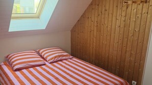 A bedroom with a sloped ceiling, wooden panel walls, a bed with striped bedding, and a skylight.