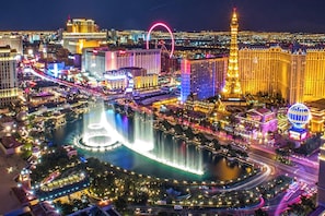 A cityscape with illuminated buildings, a prominent tower, and a large fountain.
