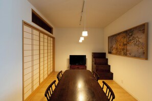 A dining room with a wooden table, chairs, a television, a painting, and a shoji screen. - WAMARE KIKUKAWA (Sumida City)