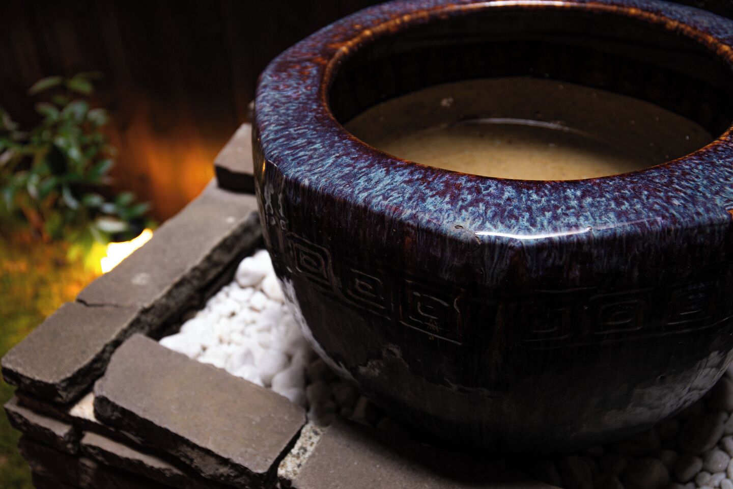 A ceramic bowl on a stone structure with a plant in the background.