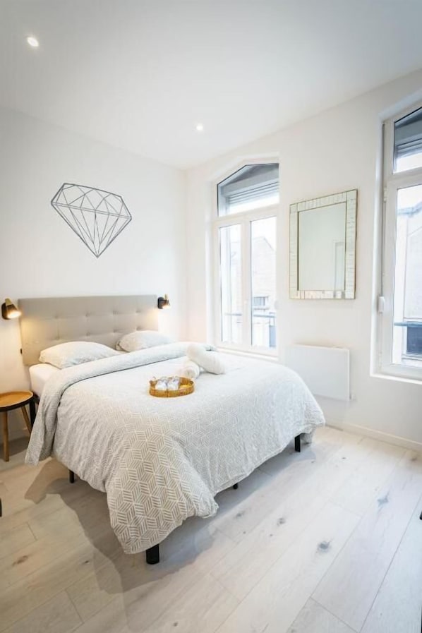Um quarto com uma cama, mesas de cabeceira, uma janela e um objeto decorativo geométrico na parede.