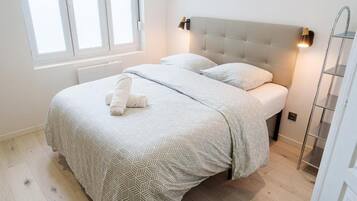 Et soveværelse med en seng, knægt, et vindue og en vægmonteret lampe.