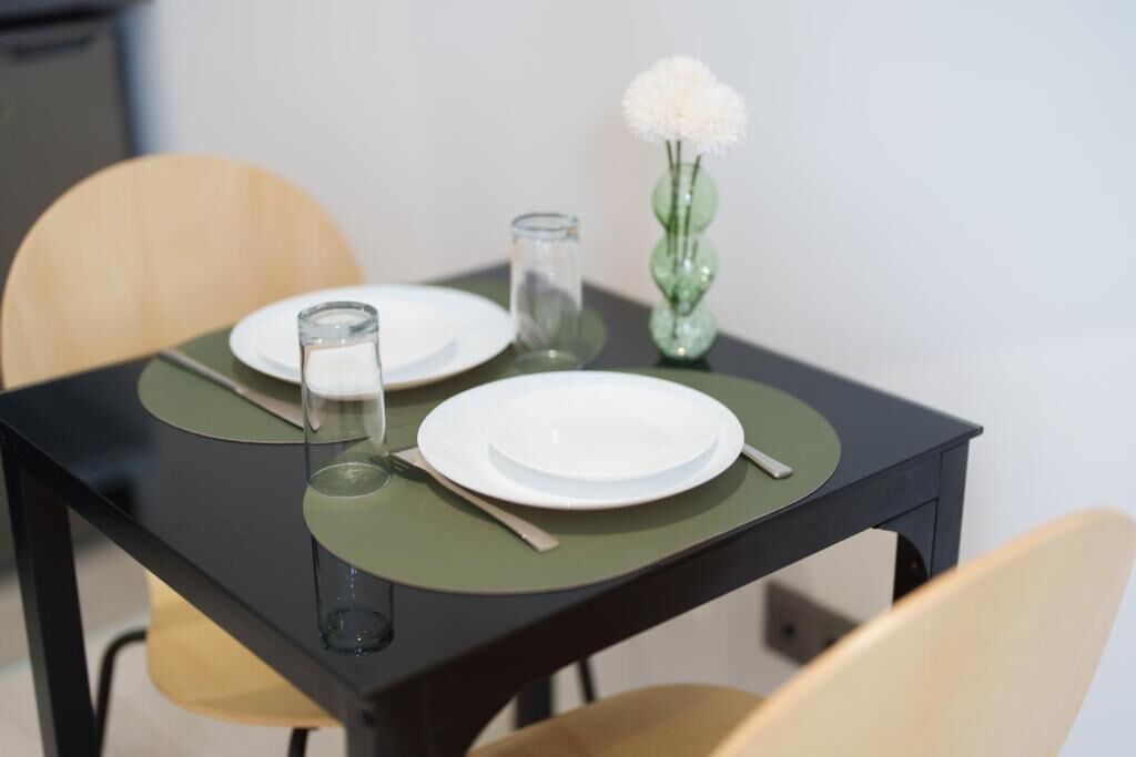 A dining table with two plates, a glass, and a vase with a flower.