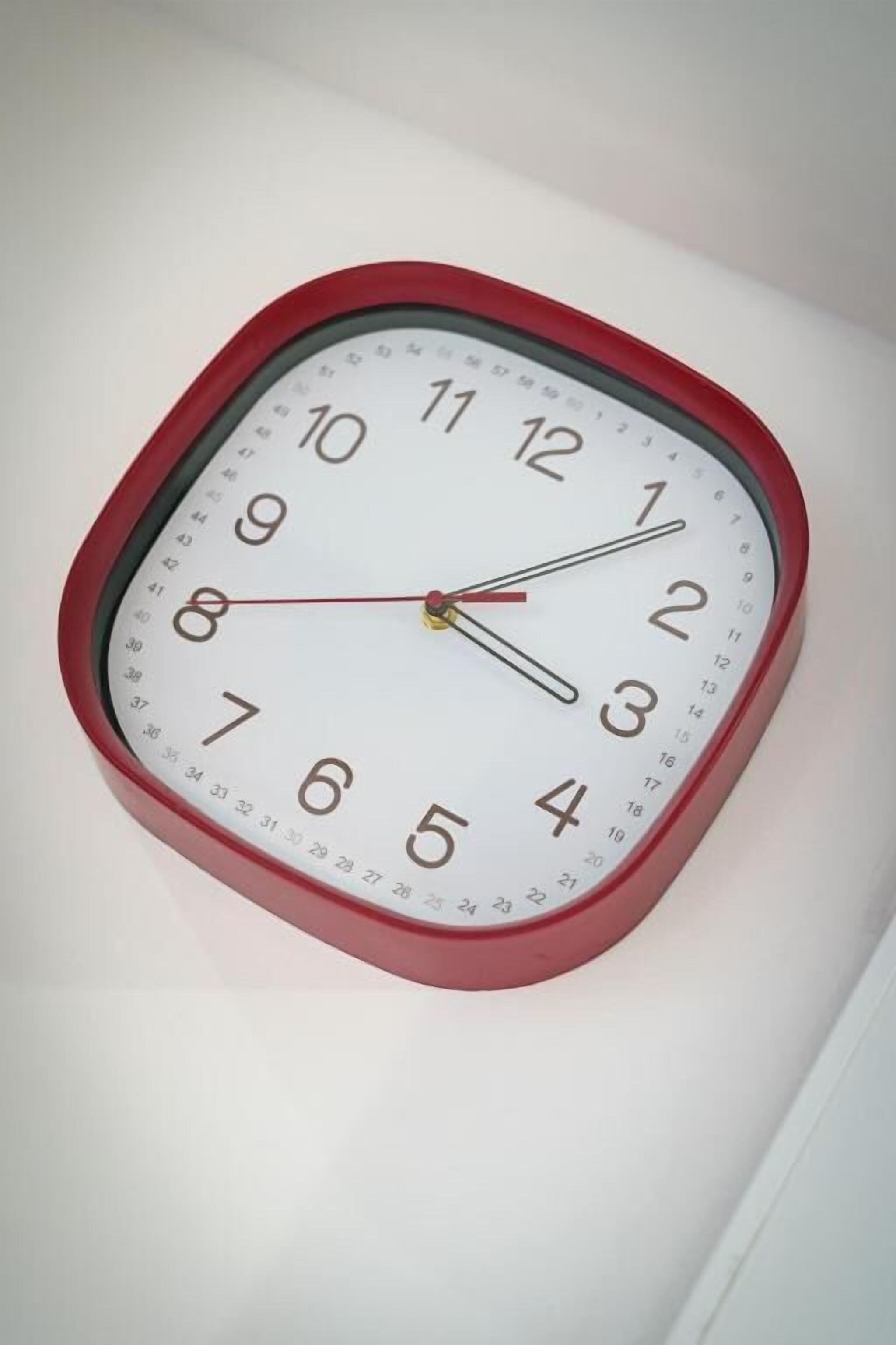 A square wall clock with a red frame and white face, displaying the time.