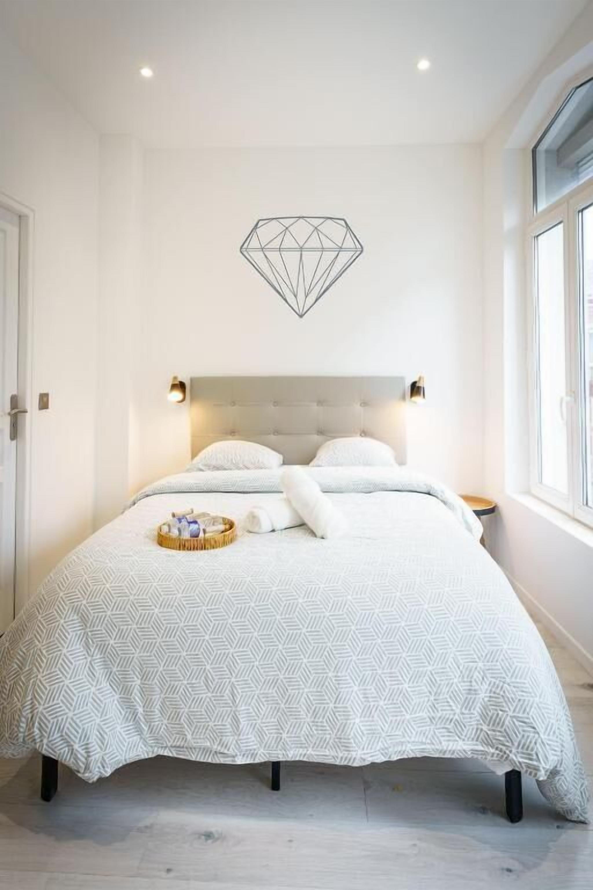 A bedroom with a bed, a wall-mounted geometric decoration, and a window.