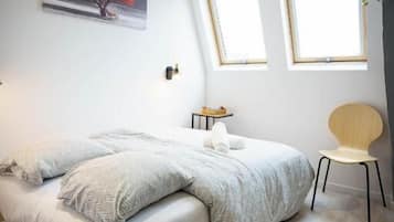 Un dormitorio con una cama, dos ventanas, una silla y un cuadro en la pared.