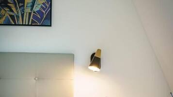 Quarto com cama, mesa de cabeceira com vaso, luminária de parede e um quadro.