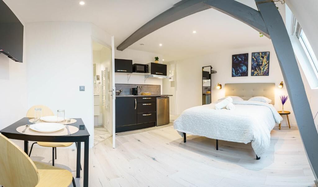 A modern bedroom with a large bed, a small kitchen area, and a dining table with chairs.