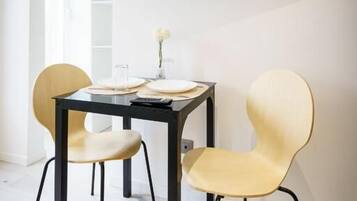 A dining area with a table, chairs, a flat-screen TV mounted on the wall, and a clock on the wall.