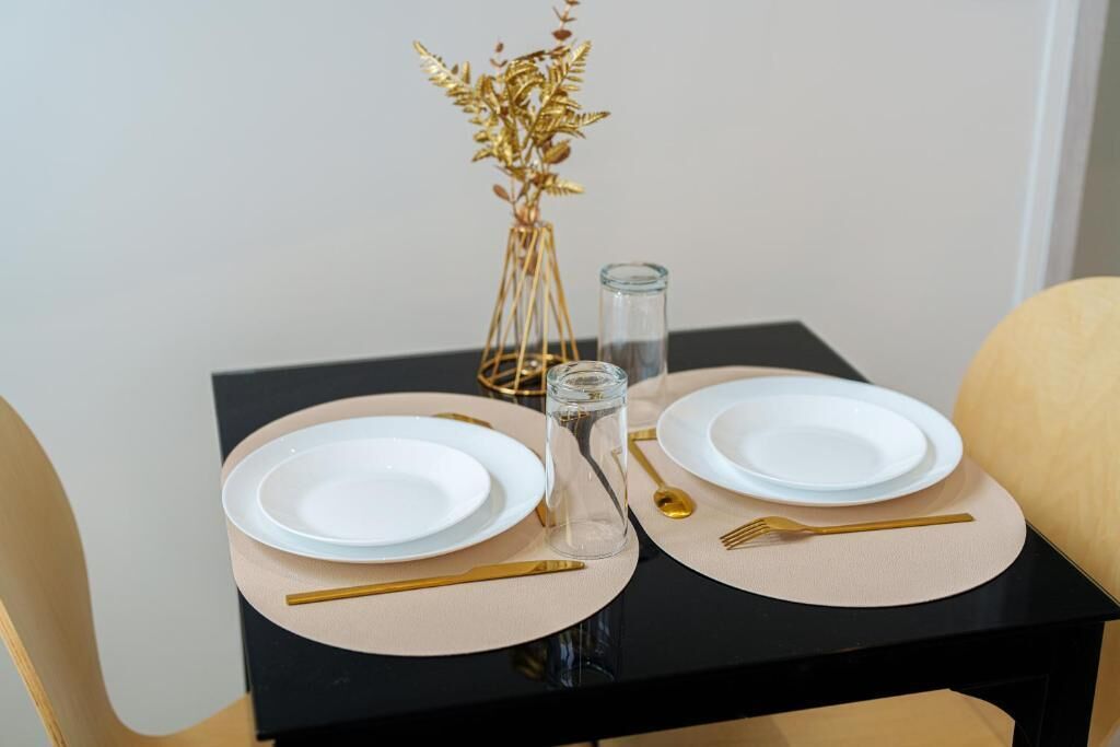 Ein Tisch ist gedeckt mit weißen Tellern, goldartigem Besteck und einer Glasvase mit goldenen Blättern.