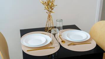 Ein Tisch ist gedeckt mit weißen Tellern, goldartigem Besteck und einer Glasvase mit goldenen Blättern.